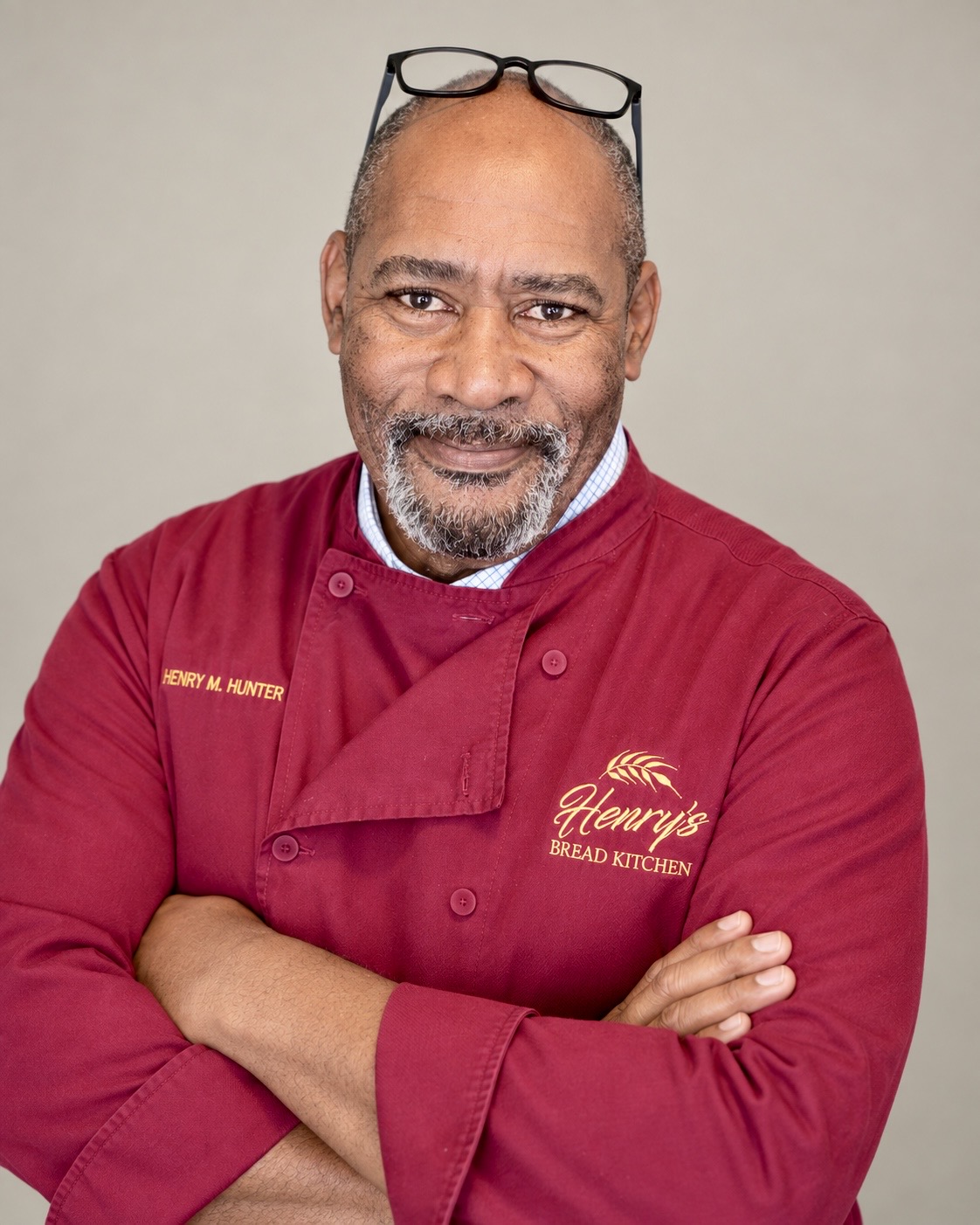 Henry Hunter, wearing his burgundy baker's coat, with his arms folded